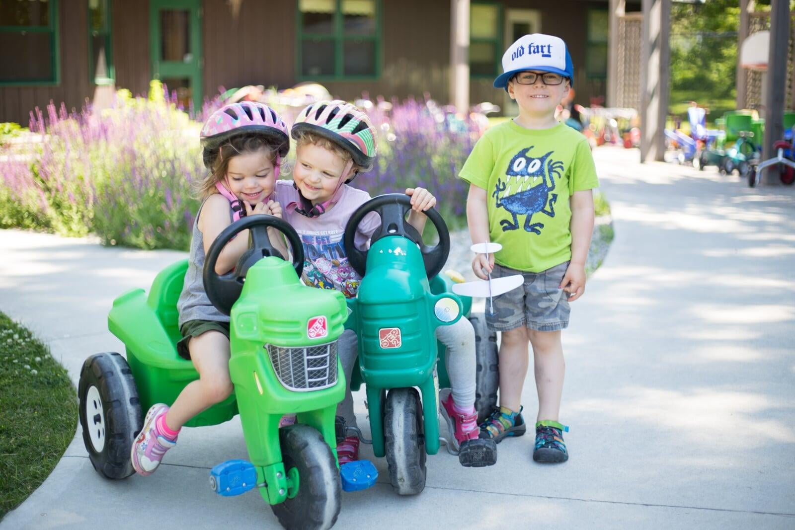 Children Playing Front Of The Hub. Two are on green bikes. One Child is standing.